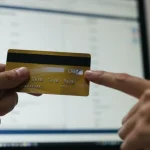 Pessoa analisando extrato de cartão de crédito em tela de computador, com foco em uma transação suspeita. Mão apontando para o item.