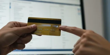 Pessoa analisando extrato de cartão de crédito em tela de computador, com foco em uma transação suspeita. Mão apontando para o item.