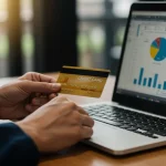 Mão segurando cartão de crédito sobre notebook com gráficos financeiros, simbolizando a gestão de um MEI.
